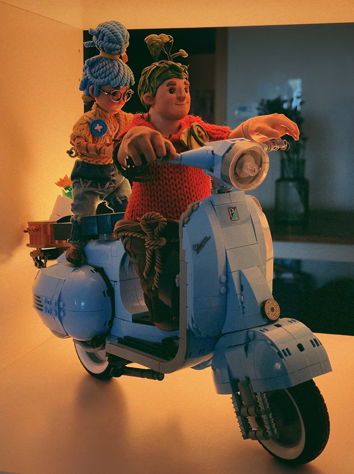 Small figures of Cody and May from the game It Takes Two standing on a blue LEGO Vespa 125 model.