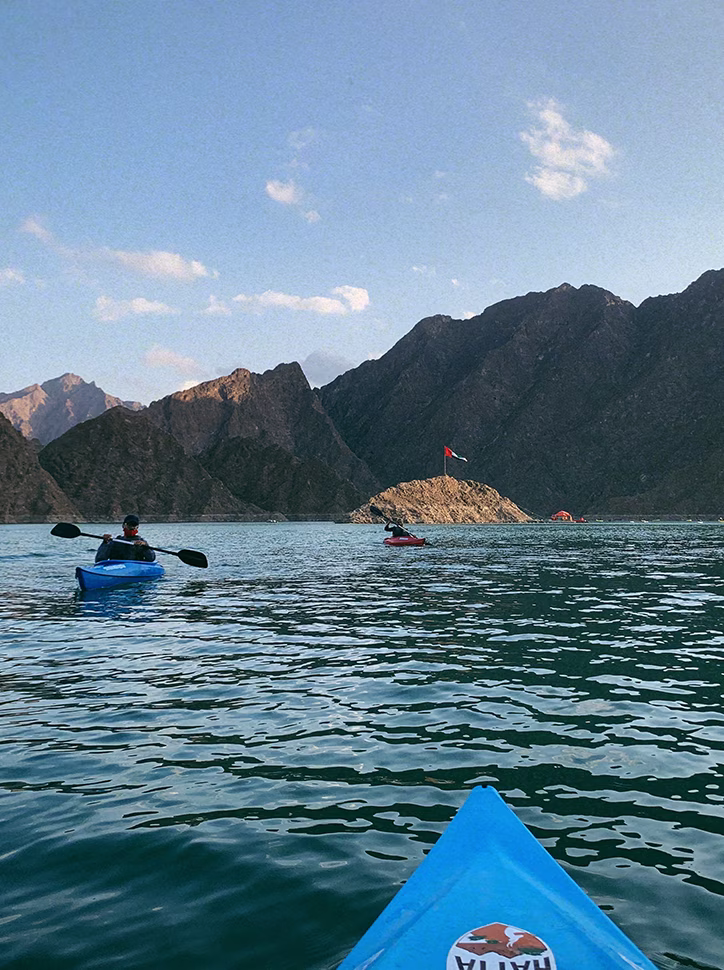 People kayaking on a calm lake surrounded by rocky mountains under a clear blue sky.